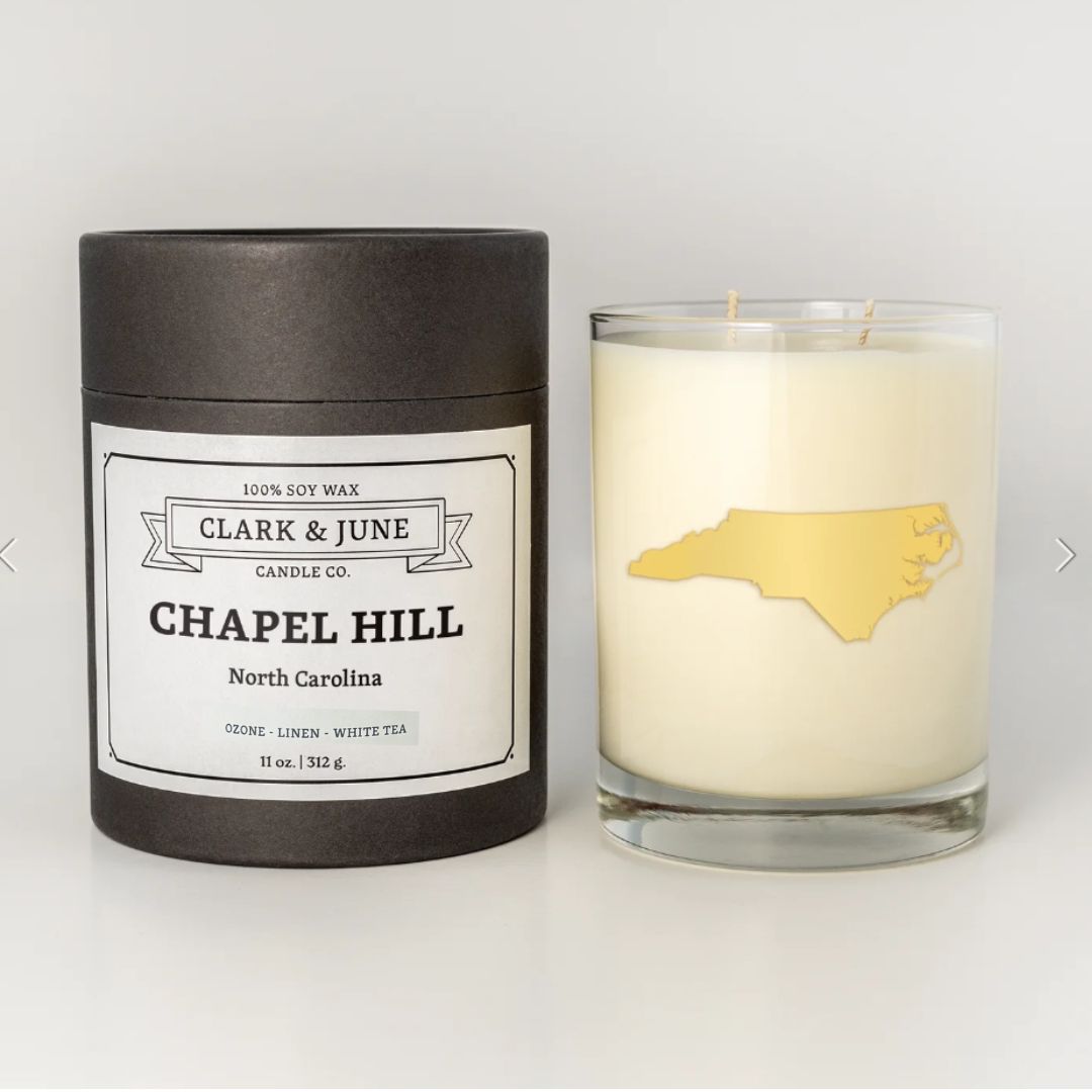 Chapel Hill candle with a 22k gold foil silhouette of North Carolina, sitting next to its elegant black tube packaging labeled 'Chapel Hill.