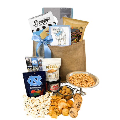 Gift Bag full of locally made in North Carolina products including Dewey's Vanilla Cookies, Carolina BBQ chips, Ellas Parma Amore Popcorn, Ram beverage napkins, Piedmont Pennies, UNC Sour gummies, UNC chocolates.