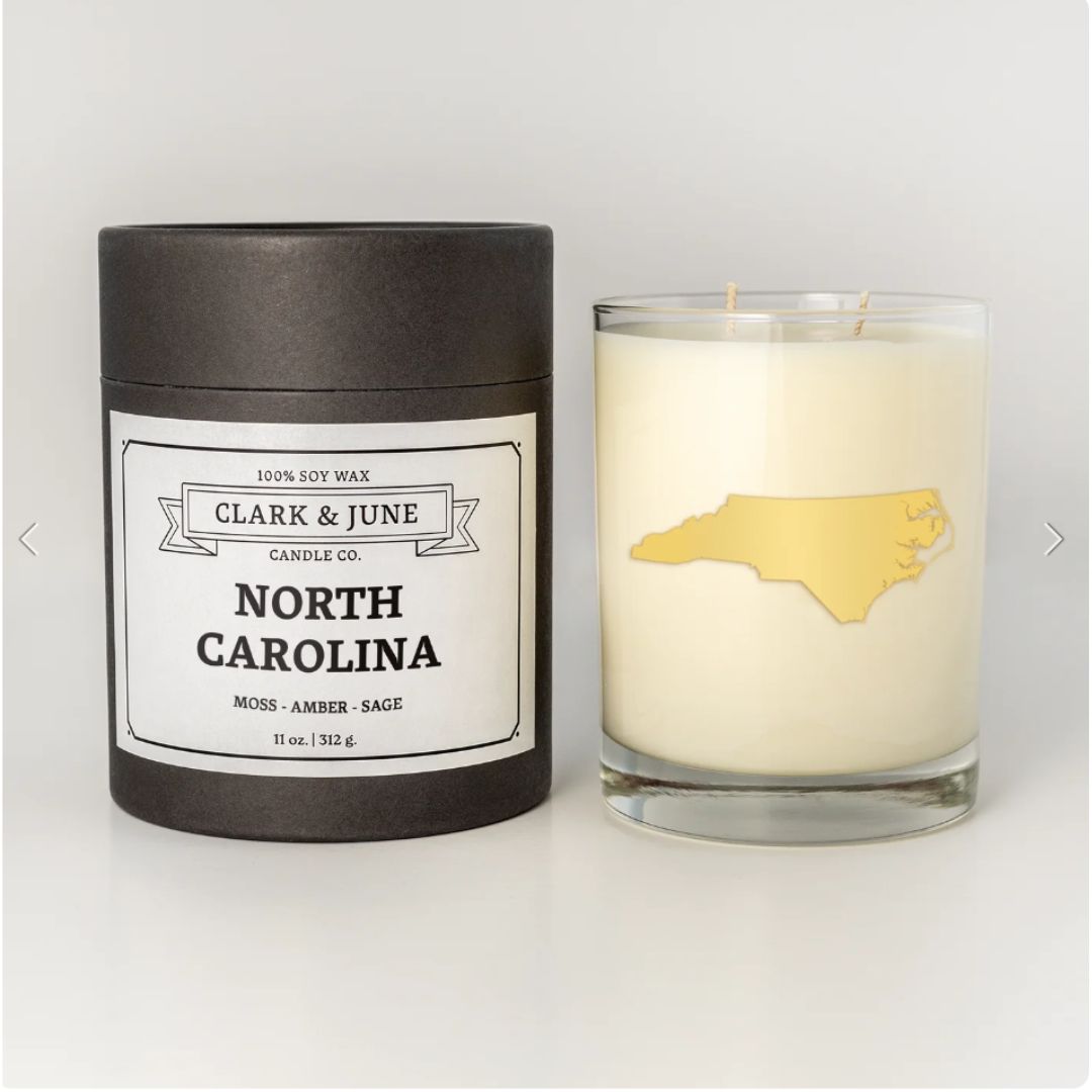 North Carolina candle with a 22k gold foil silhouette of the state, sitting next to its sleek black upscale packaging.