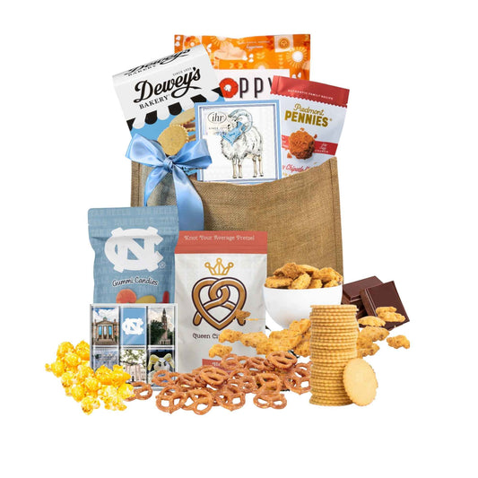 Gift Bag full of locally made in North Carolina products including Dewey's Vanilla Cookies, Carolina BBQ chips, Ellas Parma Amore Popcorn, Ram beverage napkins, Piedmont Pennies, UNC Sour gummies, UNC chocolates.