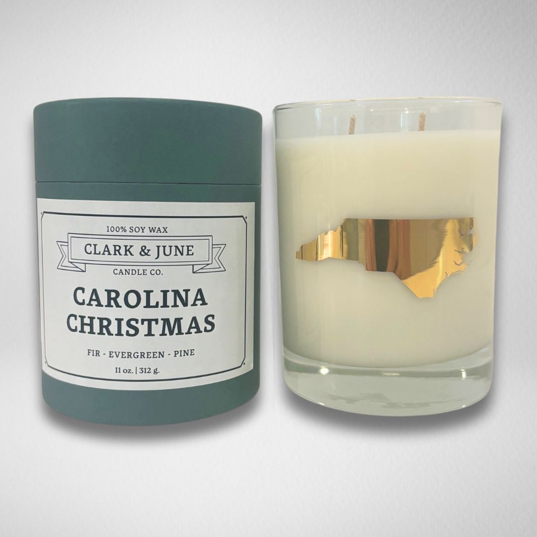 Carolina Christmas candle in a dark green tube with festive green and ivory candy stripes inside. The candle features a 22k gold foil silhouette of North Carolina on a reusable 13.5oz glass, capturing the essence of the holiday season with scents of fir, evergreen, and pine.