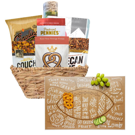 A Football Game Day Charcuterie Gift Basket featuring North Carolina-made snacks and a football-shaped charcuterie cheat sheet in front. Includes BBQ chips, spicy cheese biscuits, toffee popcorn, and more, presented in a reusable basket. Perfect for tailgates and parties.